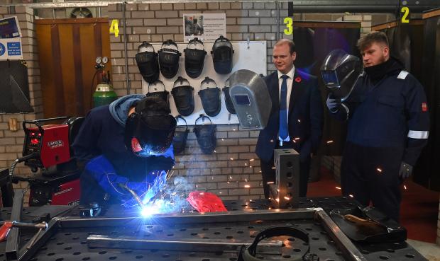Economy Minister Gordon Lyons and NRC student David McCandless watch as Gabriel Comsa of NRC carries out some welding.