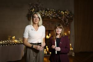 Two women hold candles at memorial event.